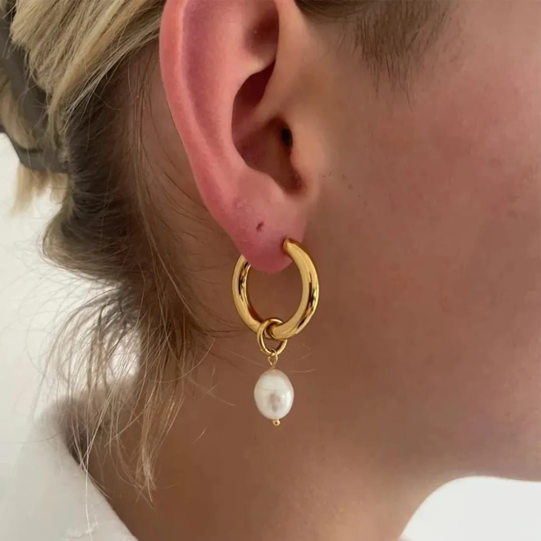 Gold hoop earring with a pearl pendant worn by a person.