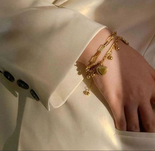 Gold bracelet with heart charm on a person wearing a white outfit.