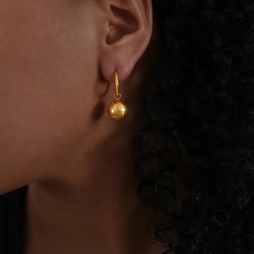 Gold earring worn by a person with a dark background pvd gold plating pvd technology goldess jewellery