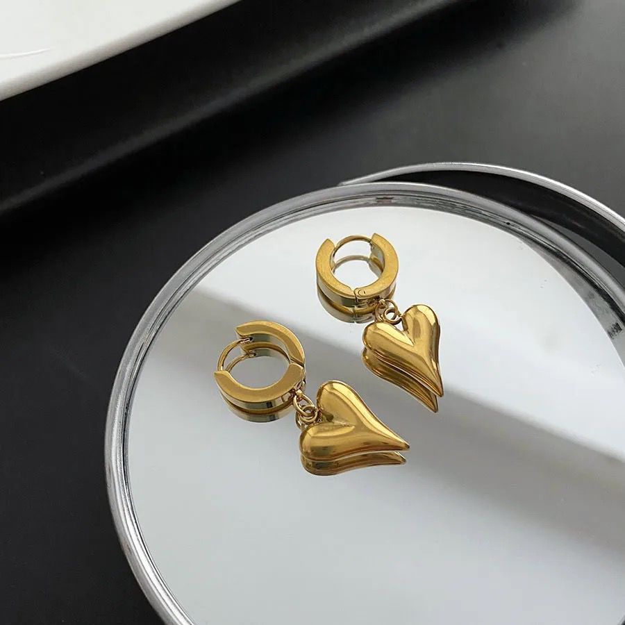 Gold heart-shaped earrings on a reflective surface which is pvd gold plated which las 10 times longer