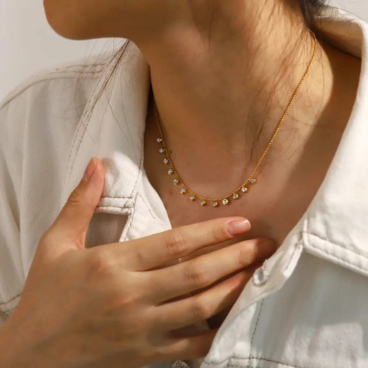 Close-up of a person wearing a delicate gold necklace with small stones, with a hand touching the chest. Goldess Jewelley 18k pure gold plated necklace trending