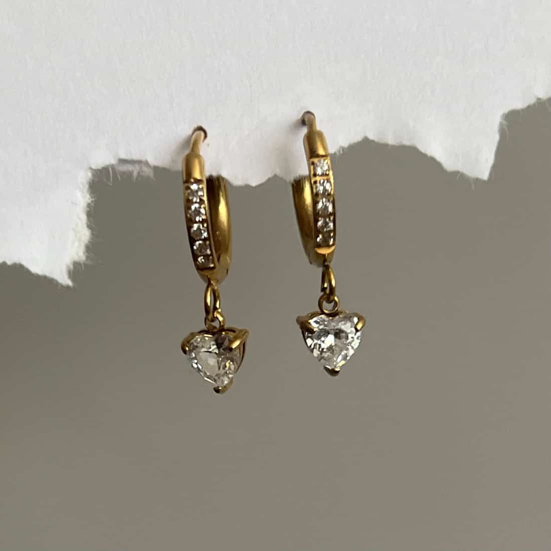 Gold hoop earrings with heart-shaped gemstones on a plain Goldess Jewelley earrings pvd technology background