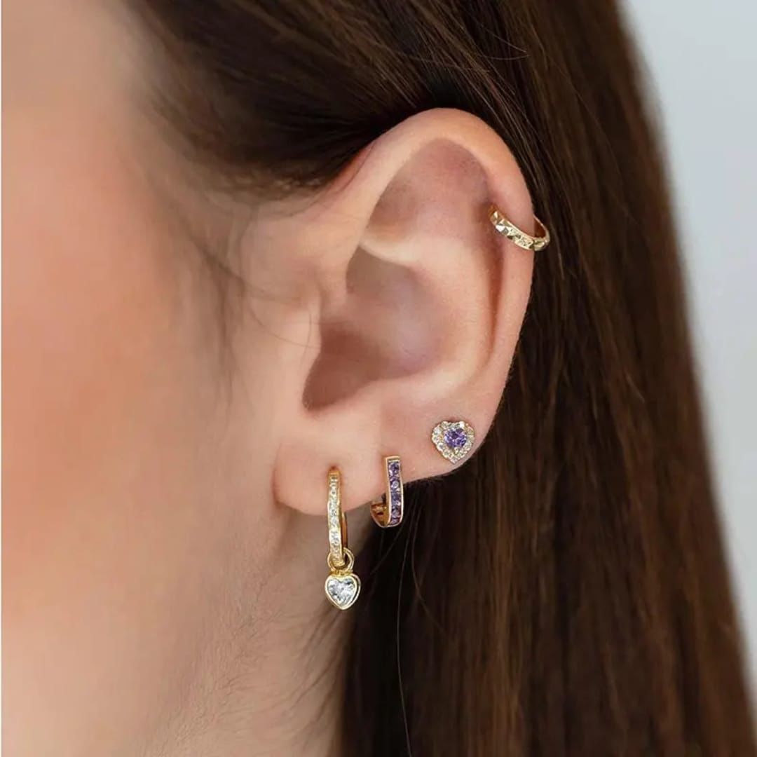 Close-up of an ear with multiple gold earrings on a neutral background Goldess Jewelley pdv earrings 18k pure gold