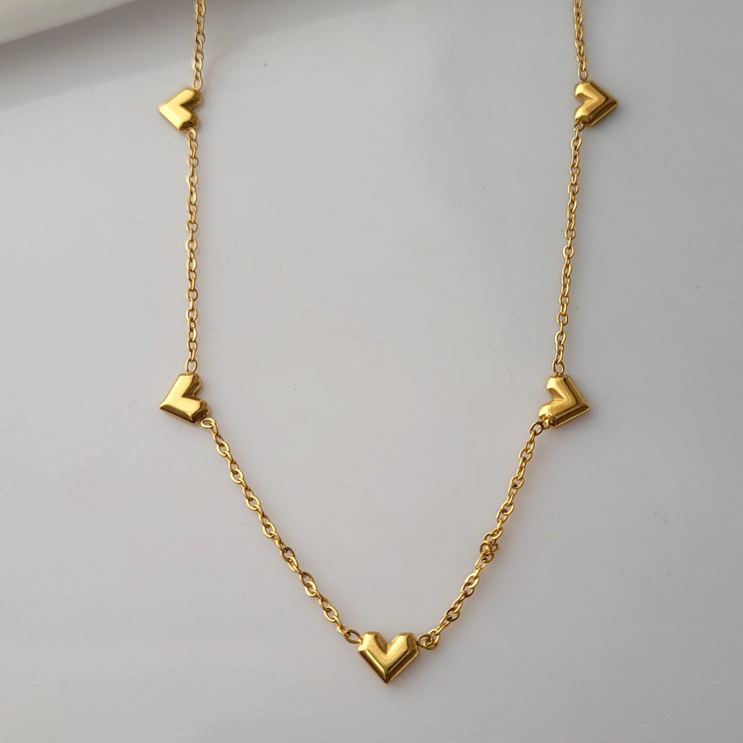 Gold necklace with heart-shaped pendants on a light gray background Goldess Jewellry with pvd plating technology which last 10 times than norlam jewelley