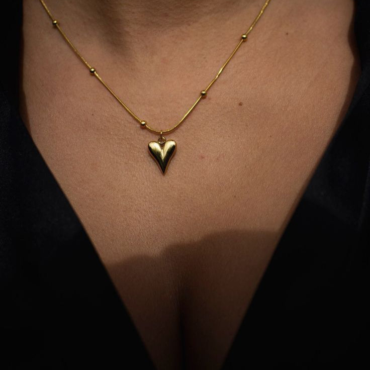Gold necklace with a heart pendant on a person against a dark Goldess demi fine jewellery pure 18k gold platedbackground
