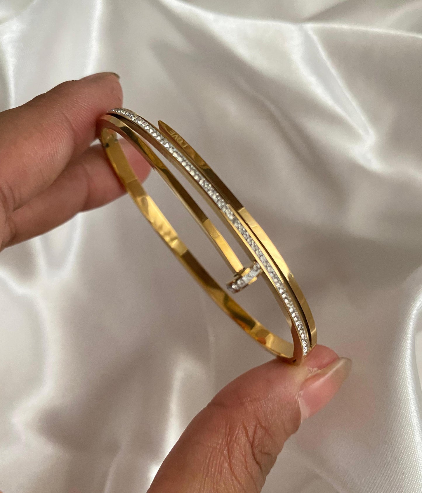 Gold bangle with diamond accents held by a hand on a white satin background