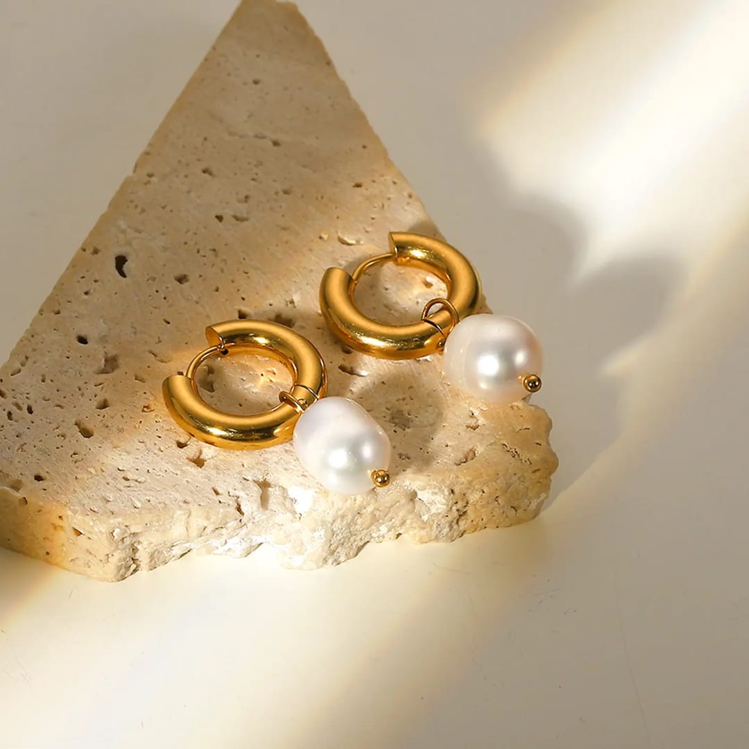 Gold hoop earrings with white pearls on a textured stone surface