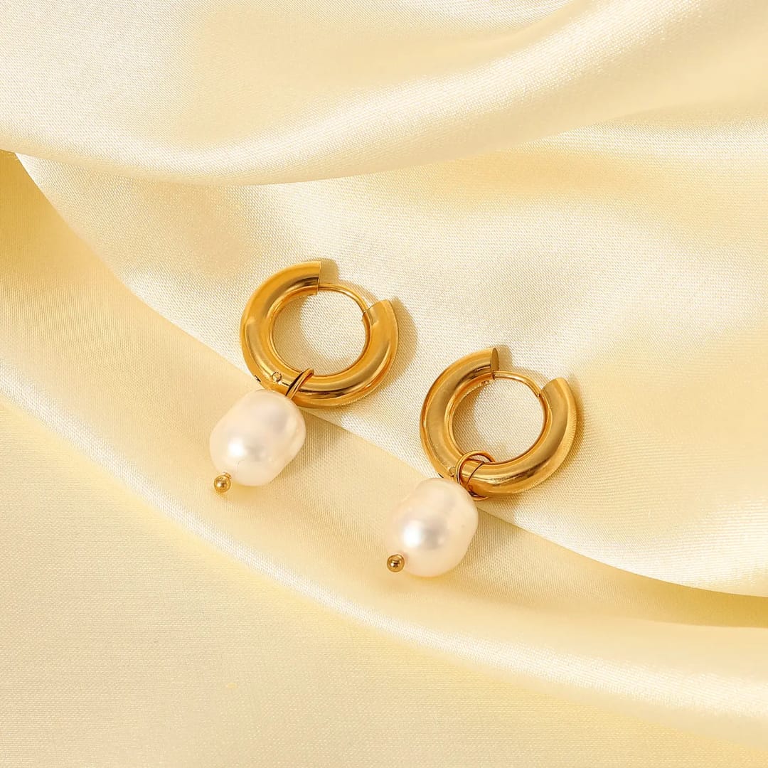 Gold hoop earrings with pearls on a beige fabric background