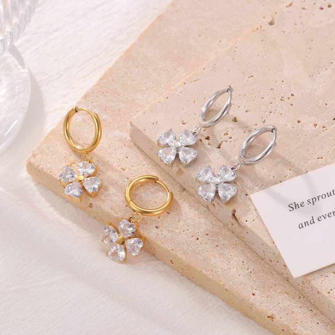 Gold and silver earrings with clear stones on a beige stone surface. Gold_plated_earring_anti_tarnish