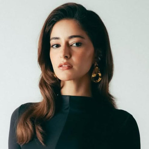 Woman wearing a black long-sleeve top with cut-out design and black skirt against a white background Goldess Jewellery Demi fine jewellry 18k gold