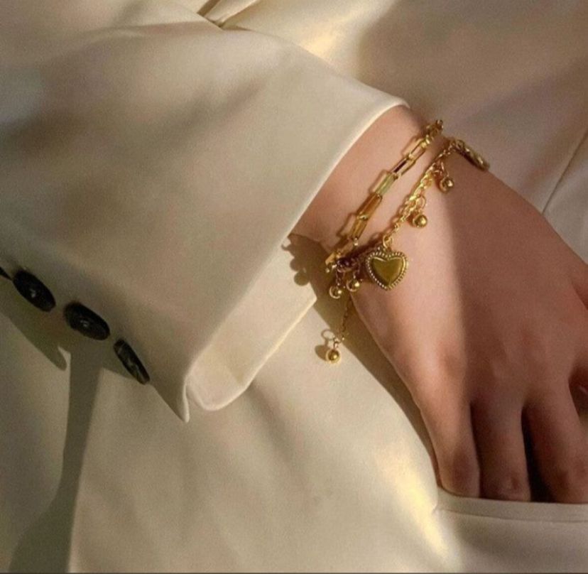 Gold bracelet with heart charm on a person wearing a white outfit.