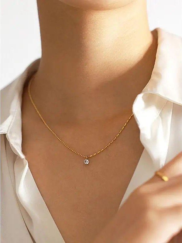 Gold necklace with a small pendant worn by a person in a white shirt. Goldess Jewellery gold plated jewelley with pvd technology