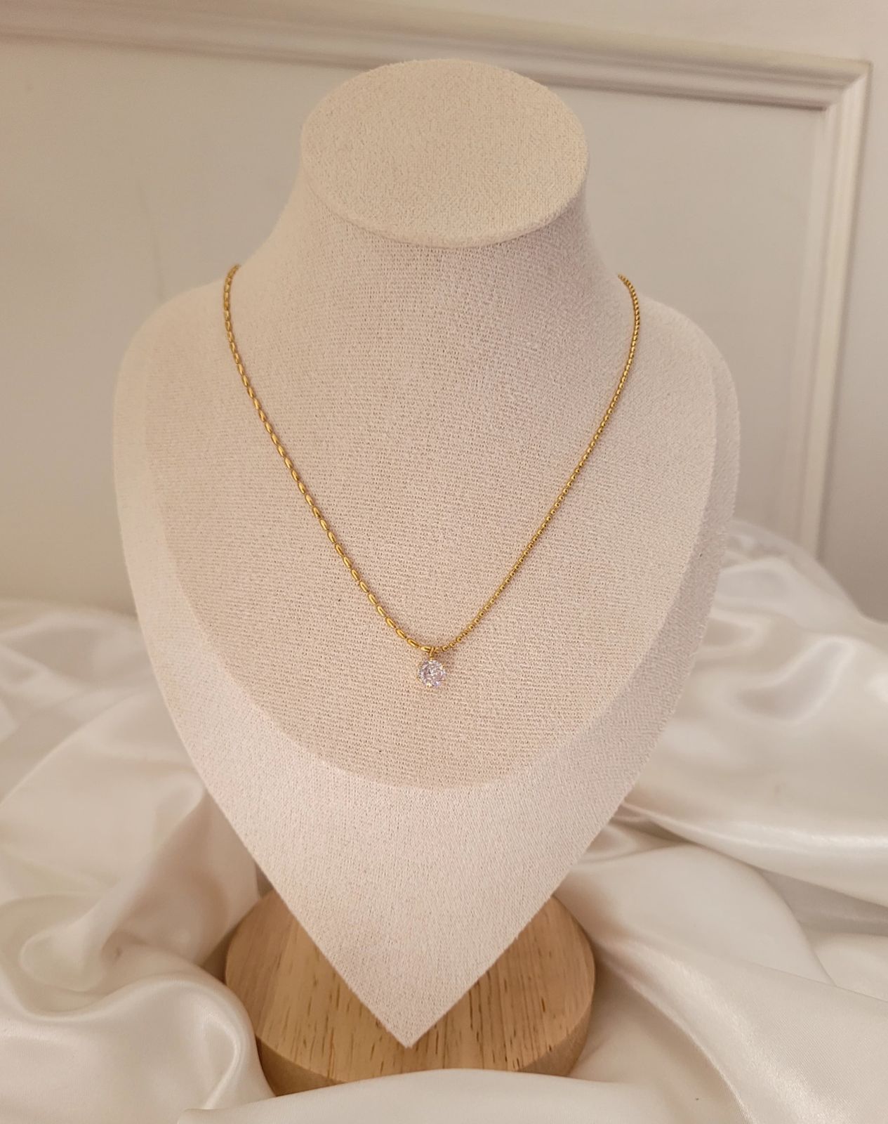 Gold necklace with a clear gemstone on a mannequin bust against a neutral background Goldess Jewellery gold plated jewelley with pvd technology