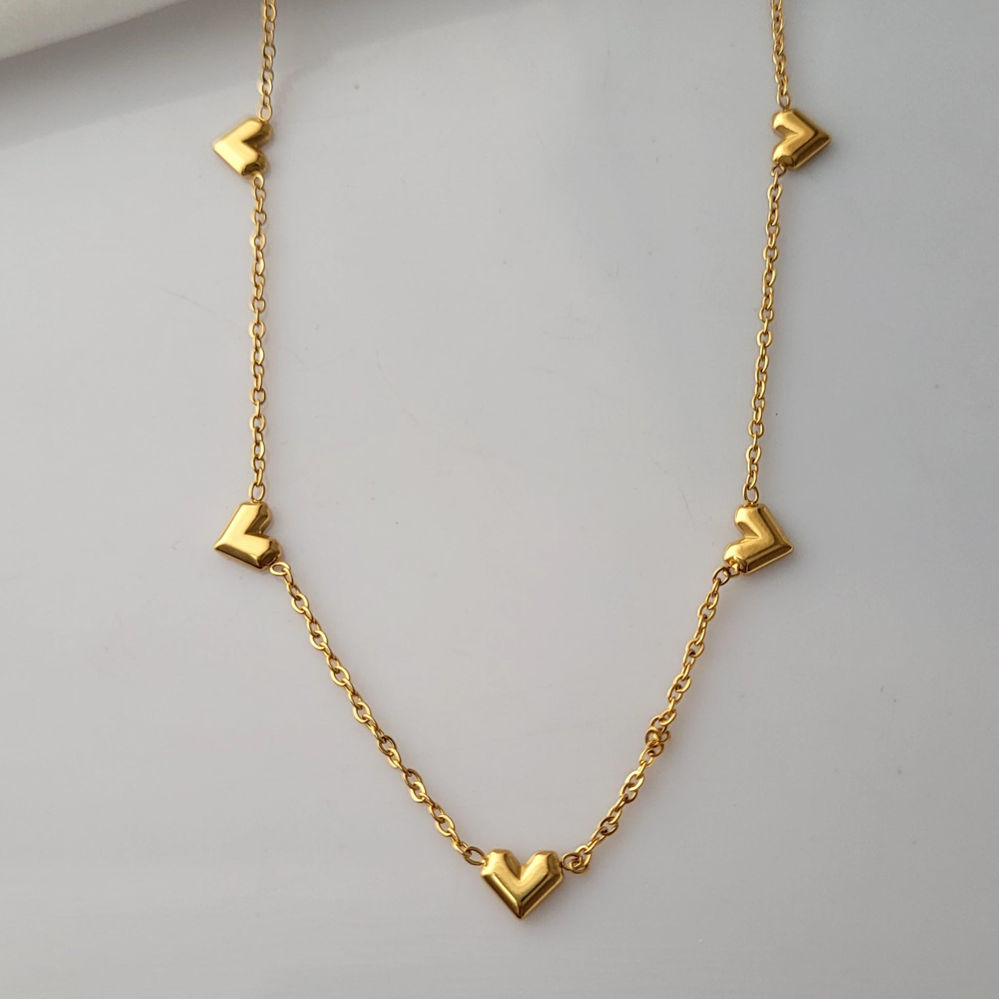 Gold necklace with heart-shaped pendants on a light gray background Goldess Jewellry with pvd plating technology which last 10 times than norlam jewelley