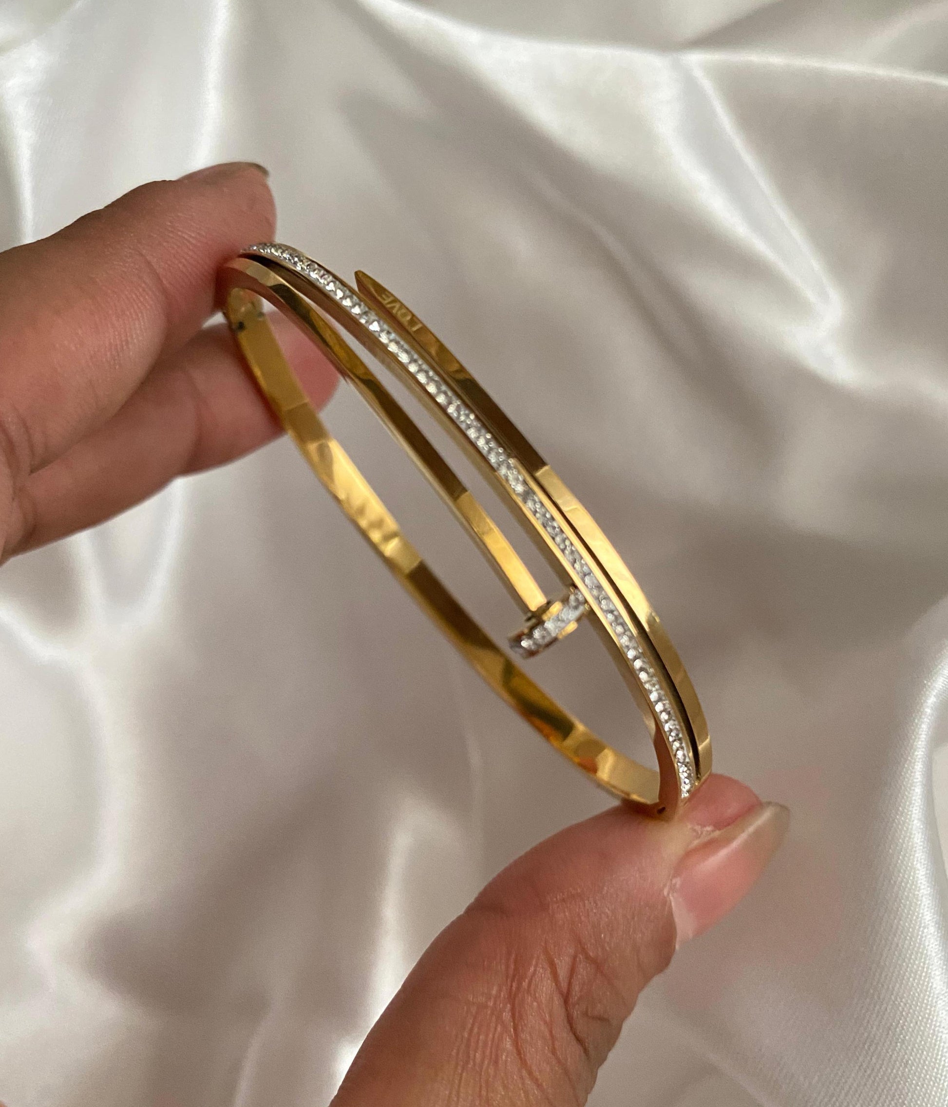 Gold bangle with diamond accents held by a hand on a white satin background