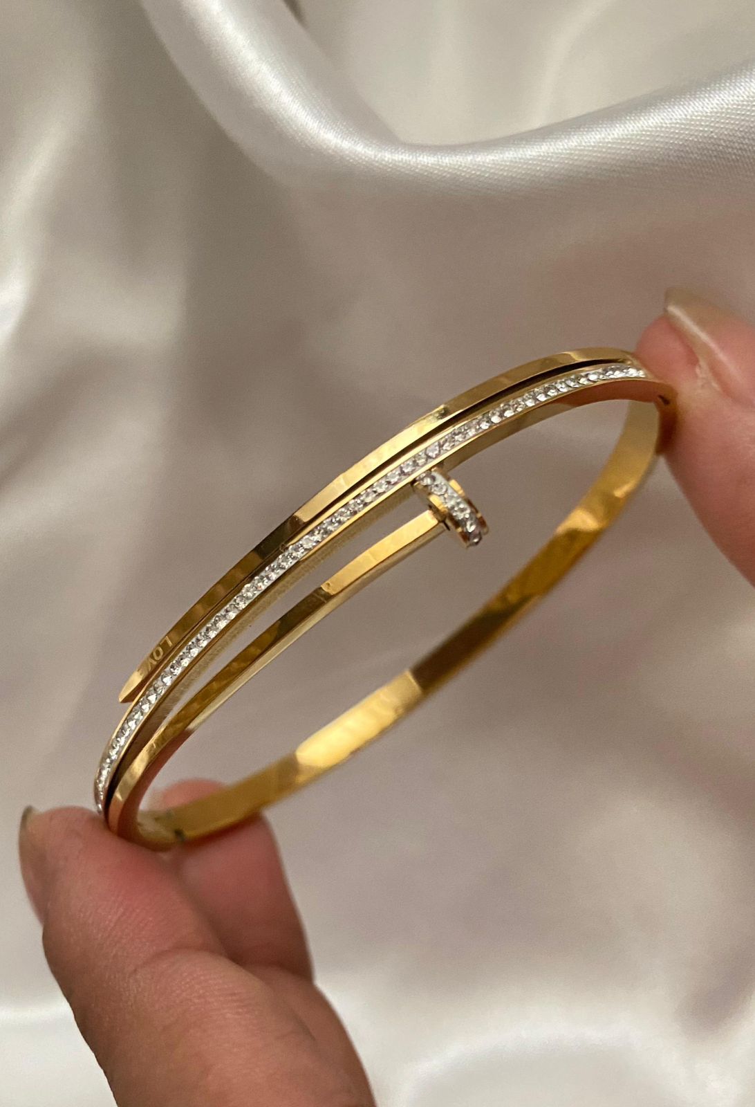 Gold bangle with diamonds held by a hand on a white background